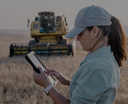 A girl with a tablet computer is standing on a crop field near a harvester.