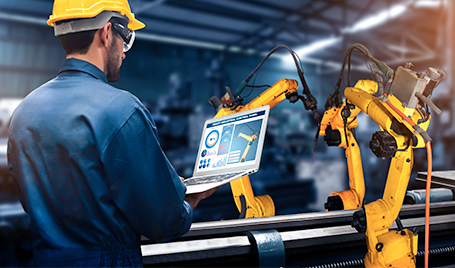 An engineer controls the operations of robotic manufacturing equipment using a laptop.