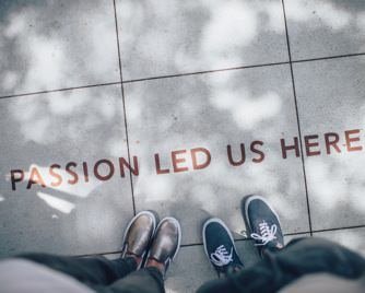 Two persons are looking at a writing on paving tiles saying ‘Passion led us here.’