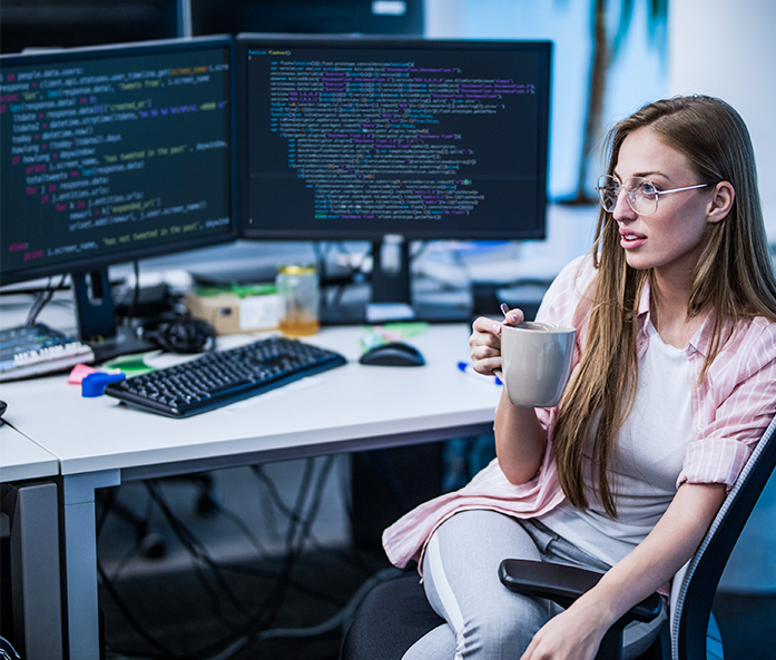 A woman sitting at a computer and drinking coffee from a mug.
