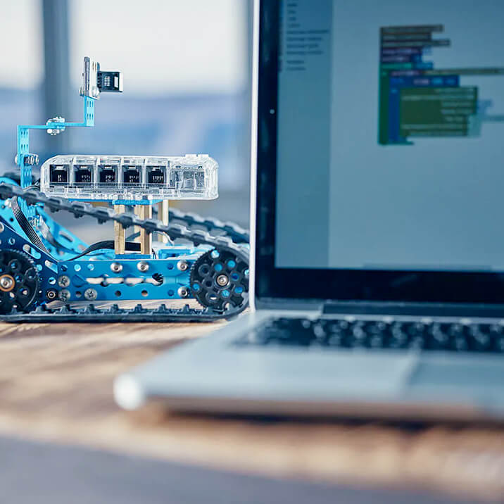 A laptop in the foreground and a small robotic device in the background