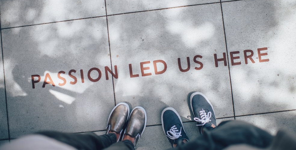 Two persons are looking at a writing on paving tiles saying ‘Passion led us here.’